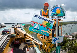 Rudy Nichols, a Florida Department of Transportation sign crew leader, positions a placard designating the Florida Keys Overseas Highway as an All-American Road, the highest national recognition a roadway can receive.